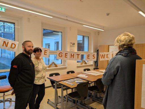 Drei Personen in einem Raum mit einem Banner im Hintergrund, auf dem „GEMEINSAM“ steht.