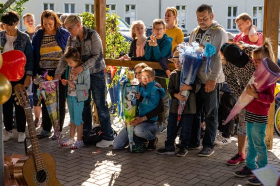 Gruppe von Menschen mit Blumen, versammelt an einem Ort, offensichtlich bei einer Gedenkfeier.