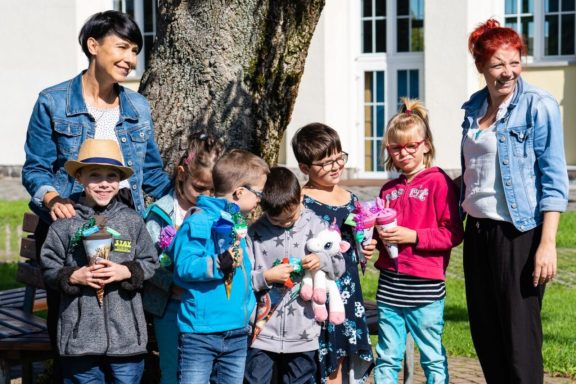 Gruppe von Kindern und Erwachsenen lächelt, während sie bunte Puppen halten.