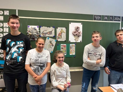 Fünf Schüler stehen vor einer Tafel mit bunten Zeichnungen.