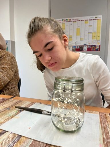 Jugendliche betrachtet ein Glas mit Wasser und Steinen auf einem Tisch.