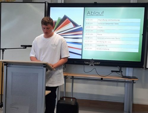Ein Jugendlicher präsentiert an einem Pult, im Hintergrund eine digitale Anzeige.