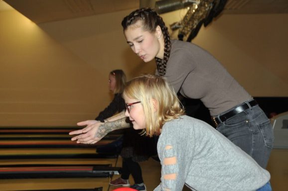 Zwei Frauen im Bowlingcenter, die gemeinsam auf die Bahn schauen und an einem Bowlingspiel teilnehmen.
