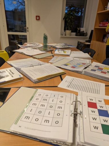 Tisch mit Lernmaterialien, Heften und Arbeitsblättern in einem Klassenraum.