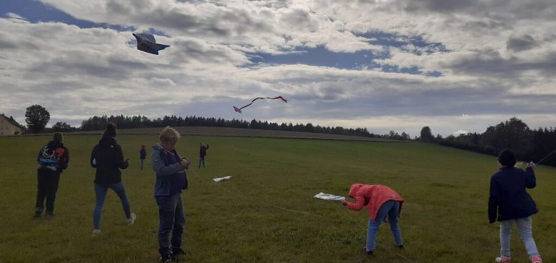 Gruppen von Menschen fliegen Drachen auf einem weiten, bewölkten Feld.