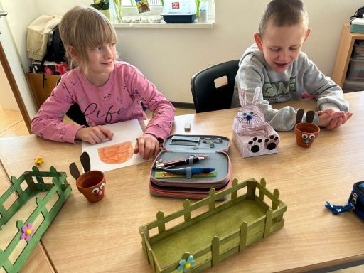 Zwei Kinder sitzen an einem Tisch und basteln mit Töpfen und Bastelmaterialien.