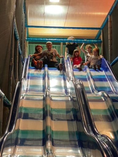 Kinder rutschen gemeinsam von einer farbigen Rutsche in einem Spielplatz.