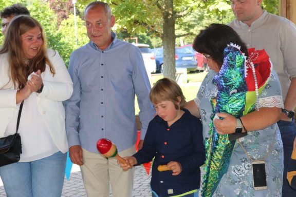 Gruppe von Menschen bei einer Feier, ein Junge hält eine Rassel und Blumen werden überreicht.