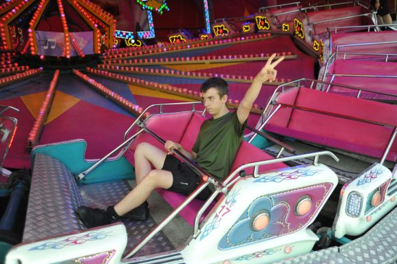 Junge sitzt in einem Fahrgeschäft und zeigt mit der Hand ein Peace-Zeichen.