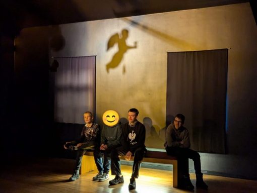 Drei Personen sitzen auf einer Bank, Schatten eines fliegenden Engels an der Wand.