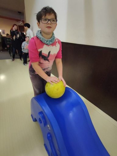 Ein Kind steht auf einer blauen Rutsche und hält eine gelbe Kugel.