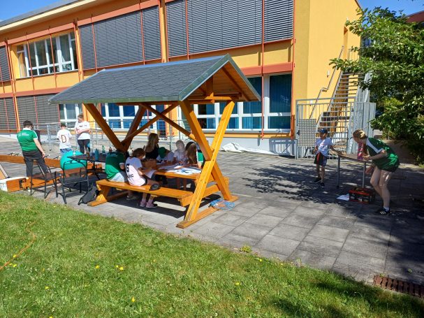Schüler und Lehrer arbeiten gemeinsam an Projekten unter einem großen Außentisch.