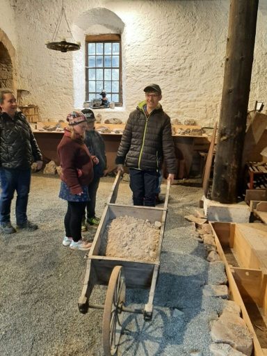 Eine Gruppe von Menschen sieht sich eine Schubkarre in einem historischen Raum an.