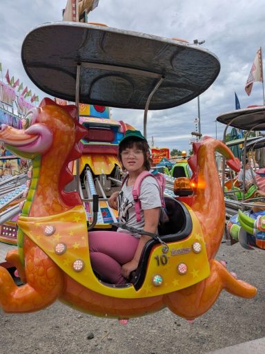 Ein Kind sitzt in einem bunten Karussell, das wie ein goldener Drache gestaltet ist.