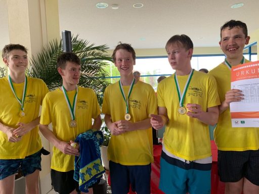 Fünf Schwimmer in gelben T-Shirts mit Medaillen posieren, einer hält ein Zertifikat.