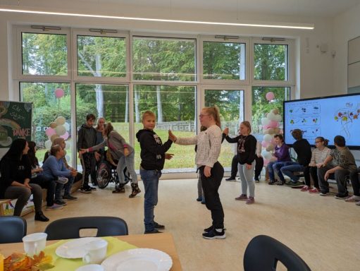 Zwei Kinder stehen in einem Raum und spielen ein Spiel, während andere zuschauen.