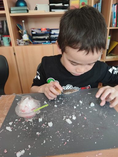 Ein Junge arbeitet an einem kreativen Projekt mit bunten Materialien auf einem Tisch.