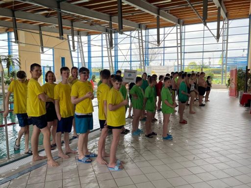 Schwimmteam in gelben und grünen T-Shirts, aufgestellt am Beckenrand.