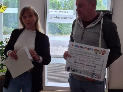 Zwei Personen halten eine Urkunde in einem Innenraum, umgeben von Pflanzen.