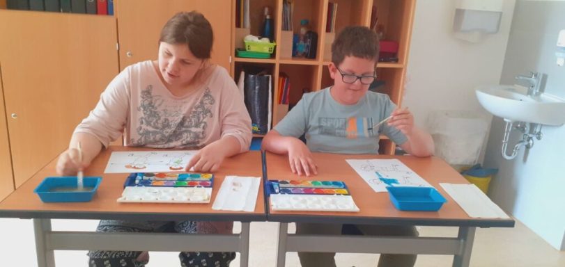 Zwei Kinder arbeiten an einem Tisch mit Lernmaterialien in einem Klassenzimmer.