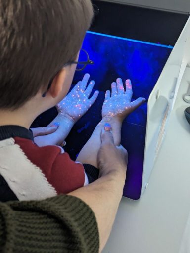 Ein Kind betrachtet seine Hände unter einer UV-Lampe, die leuchtende Punkte zeigt.