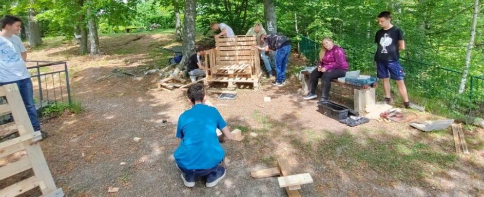 Gruppe von Personen bei handwerklichen Arbeiten im Freien, umgeben von Bäumen.