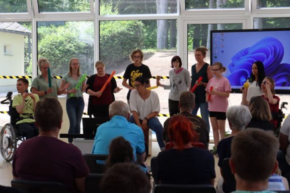 Gruppenaufführung mit Jugendlichen und Senioren in einem hellen Raum.