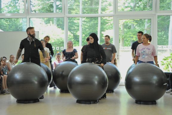 Gruppentraining mit großen Gymnastikbällen in einem hellen Raum. Zuschauer beobachten.
