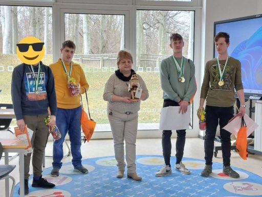 Fünf Personen in einem Raum, alle mit Medaillen und Preisen, lächeln in die Kamera.