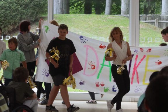 Gruppe von Menschen, die ein großes "Danke"-Banner halten und kleine Geschenke zeigen.