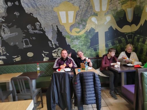 Personen sitzen in einem Café und genießen ihre Mahlzeiten vor einer Wandmalerei.