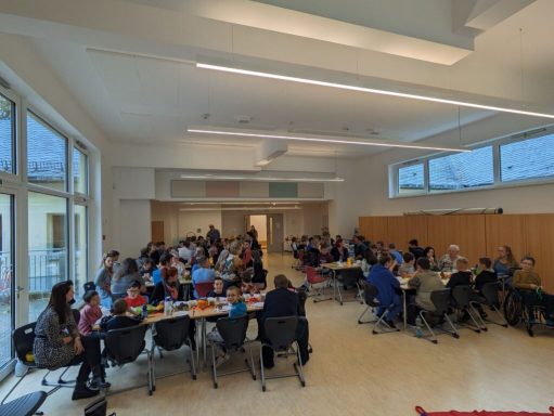 Voll besetzter Raum mit mehreren Tischen, Menschen bei einer Gruppenaktivität.