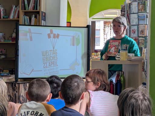 Eine Person präsentiert vor Kindern eine digitale Folie in einer Bibliothek.
